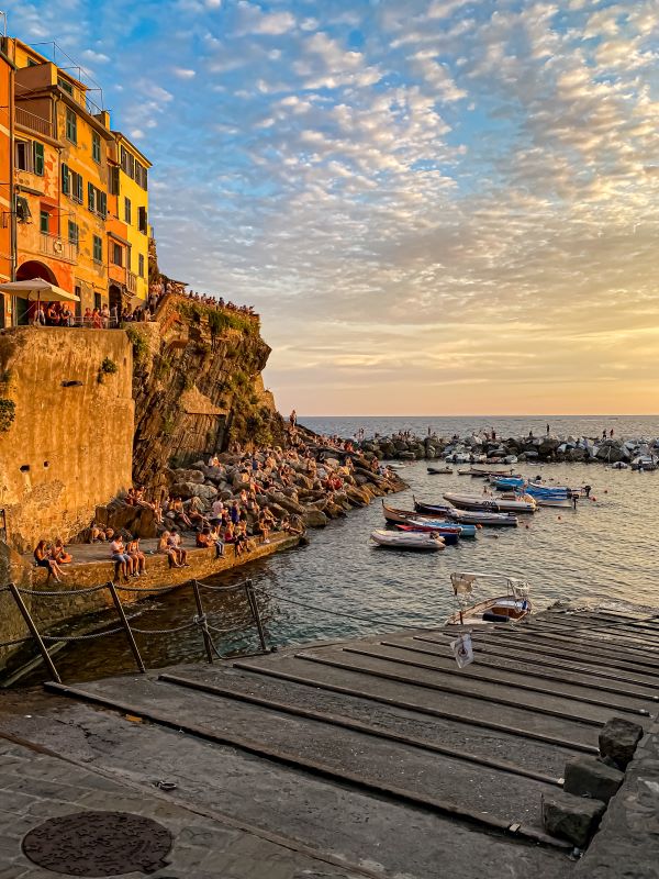 Una giornata alle Cinque Terre le persone si godono il tramonto sugli scogli del porticciolo di Riomaggiore